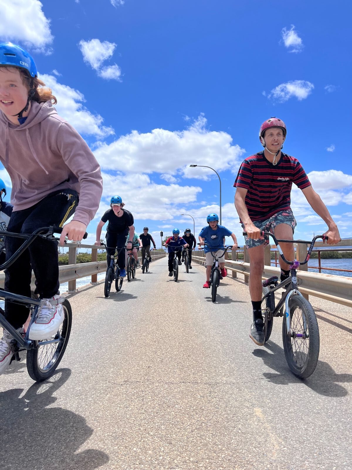 A group of cyclists riding bikes across a bridge on a sunny day, enjoying the outdoors together.