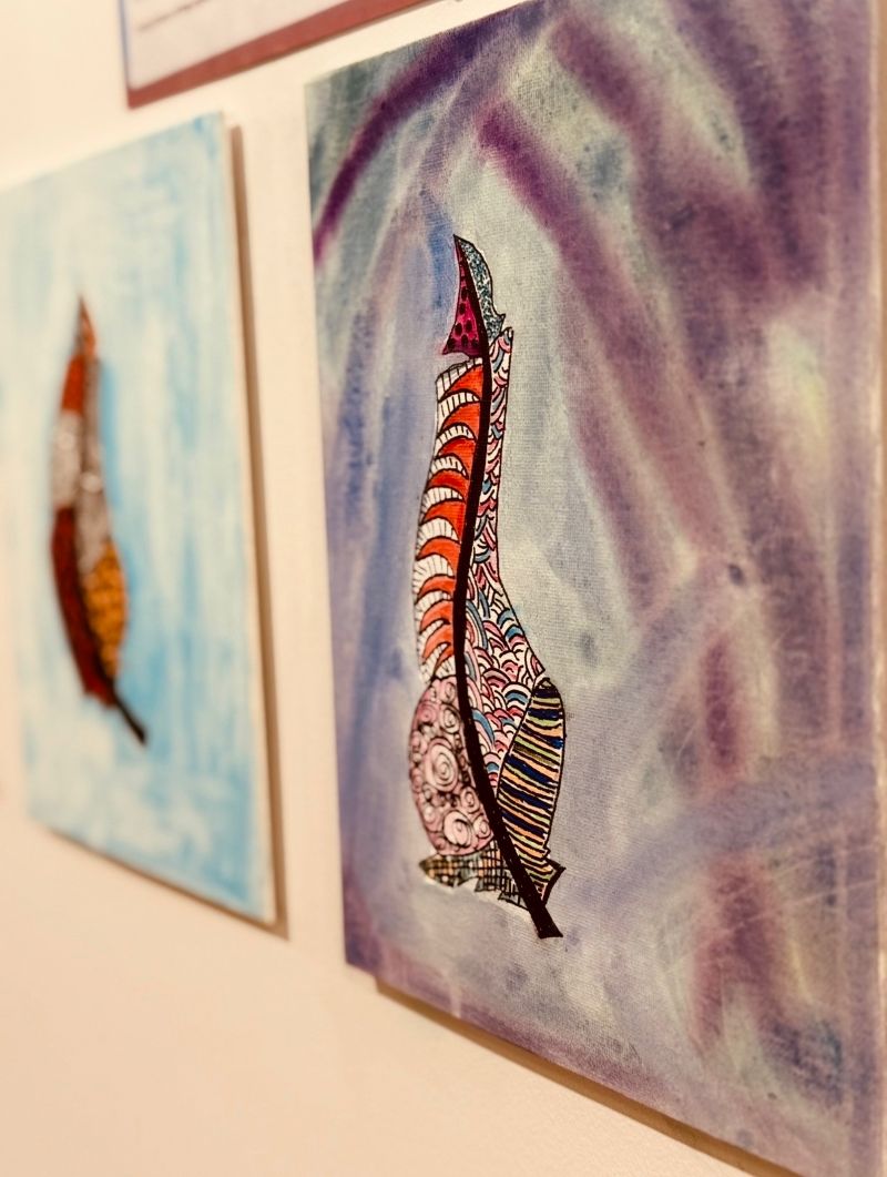 Three paintings displayed in a gallery, showcasing diverse styles and colors on white walls.