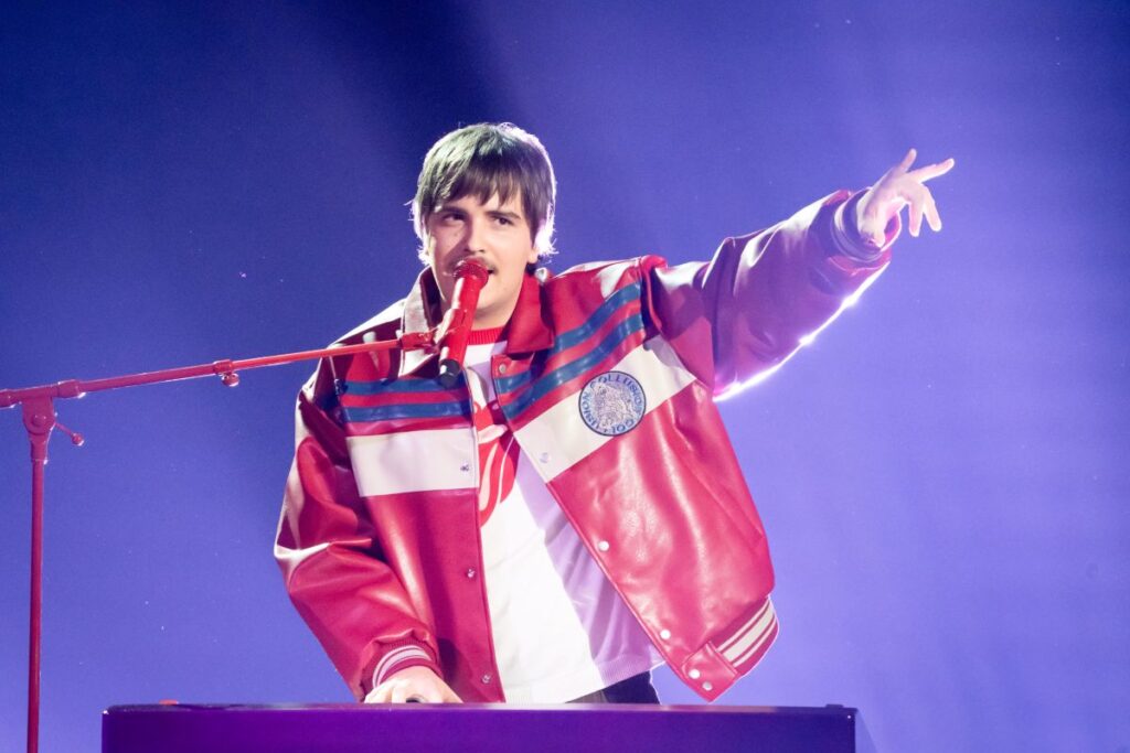 A man in a red jacket holds a microphone, ready to speak or perform.