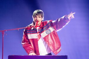 A man in a red jacket holds a microphone, ready to speak or perform.