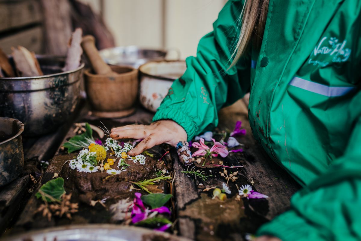 A child in a green jacket is creating a colorful flower arrangement on a table.