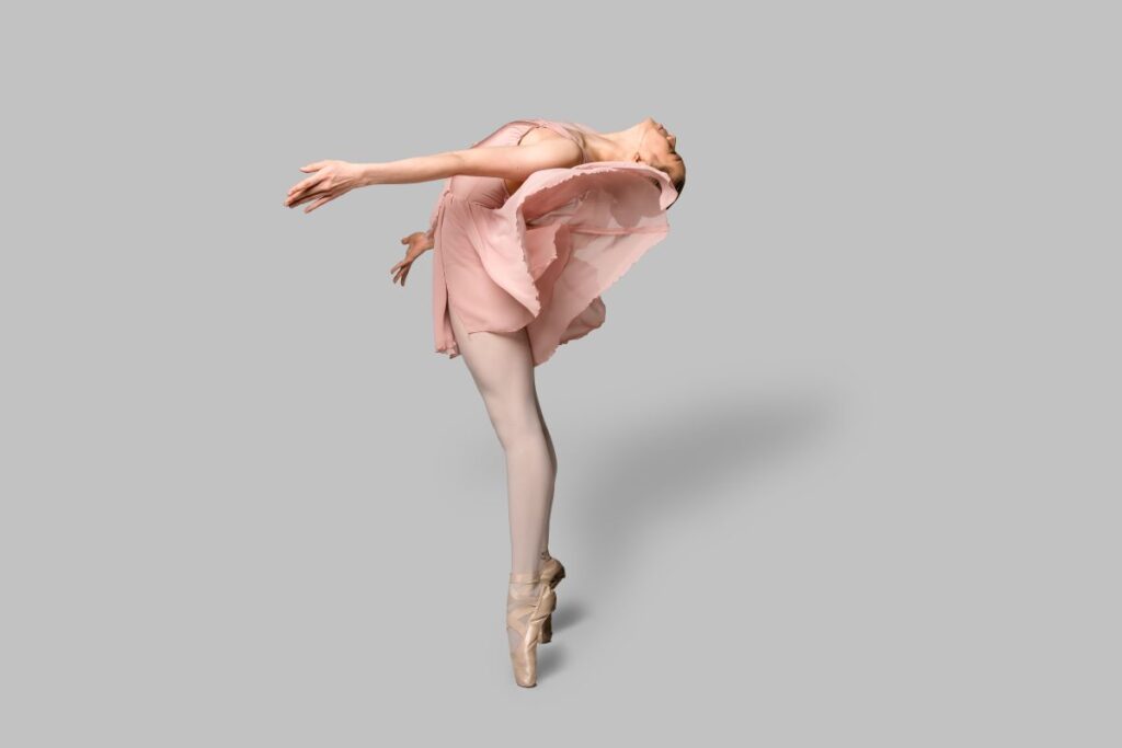 A woman in a pink dress gracefully performs a ballet pose, showcasing her elegance and poise.