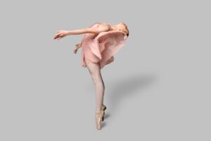 A woman in a pink dress gracefully performs a ballet pose, showcasing her elegance and poise.