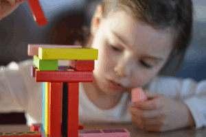 A young girl joyfully stacking colorful blocks on a table, showcasing her creativity and playfulness.