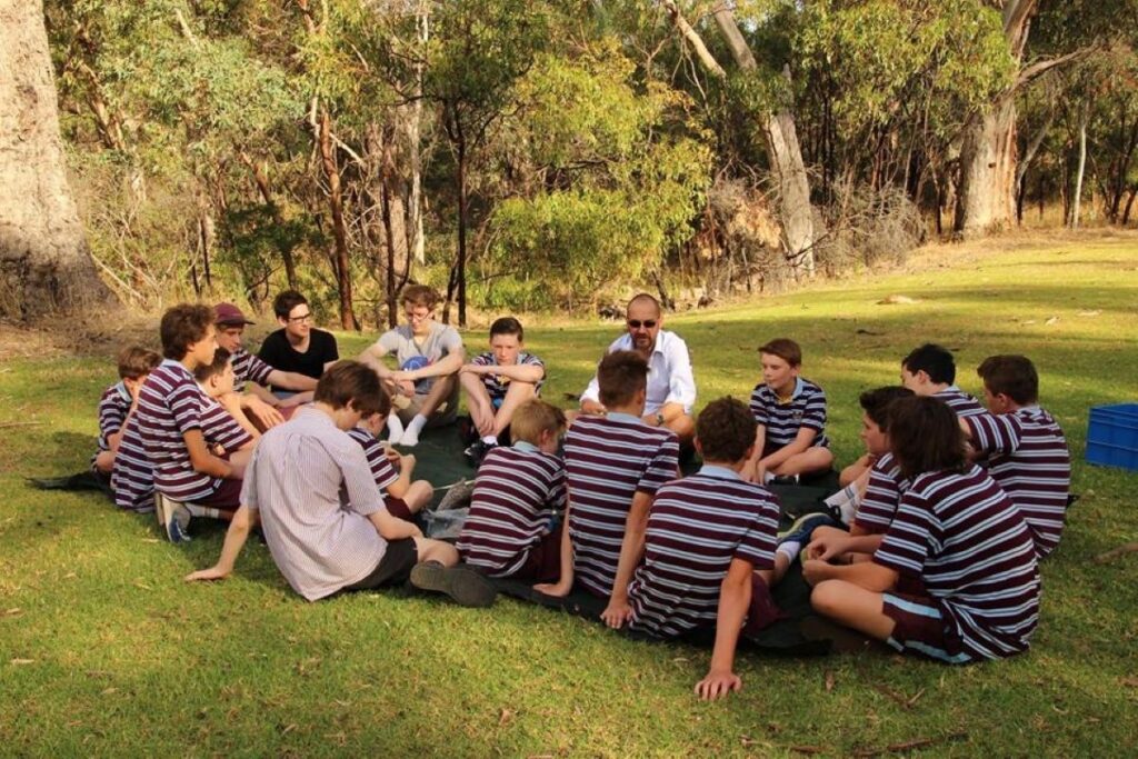 A group of students sitting in a circle on the grass, engaged in discussion and enjoying the outdoors together.