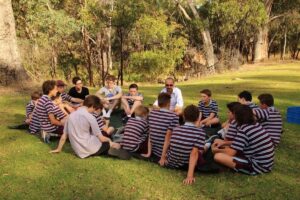 A group of students sitting in a circle on the grass, engaged in discussion and enjoying the outdoors together.