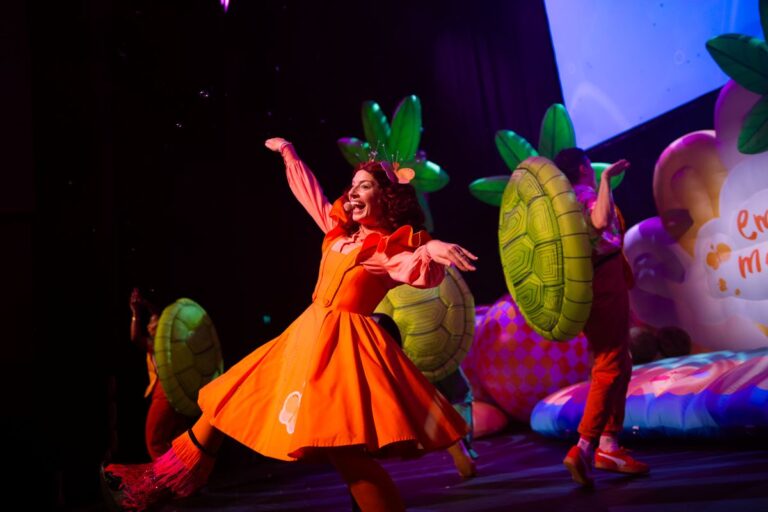 A woman in an orange dress gracefully dances on stage, showcasing her talent and energy in a vibrant performance.