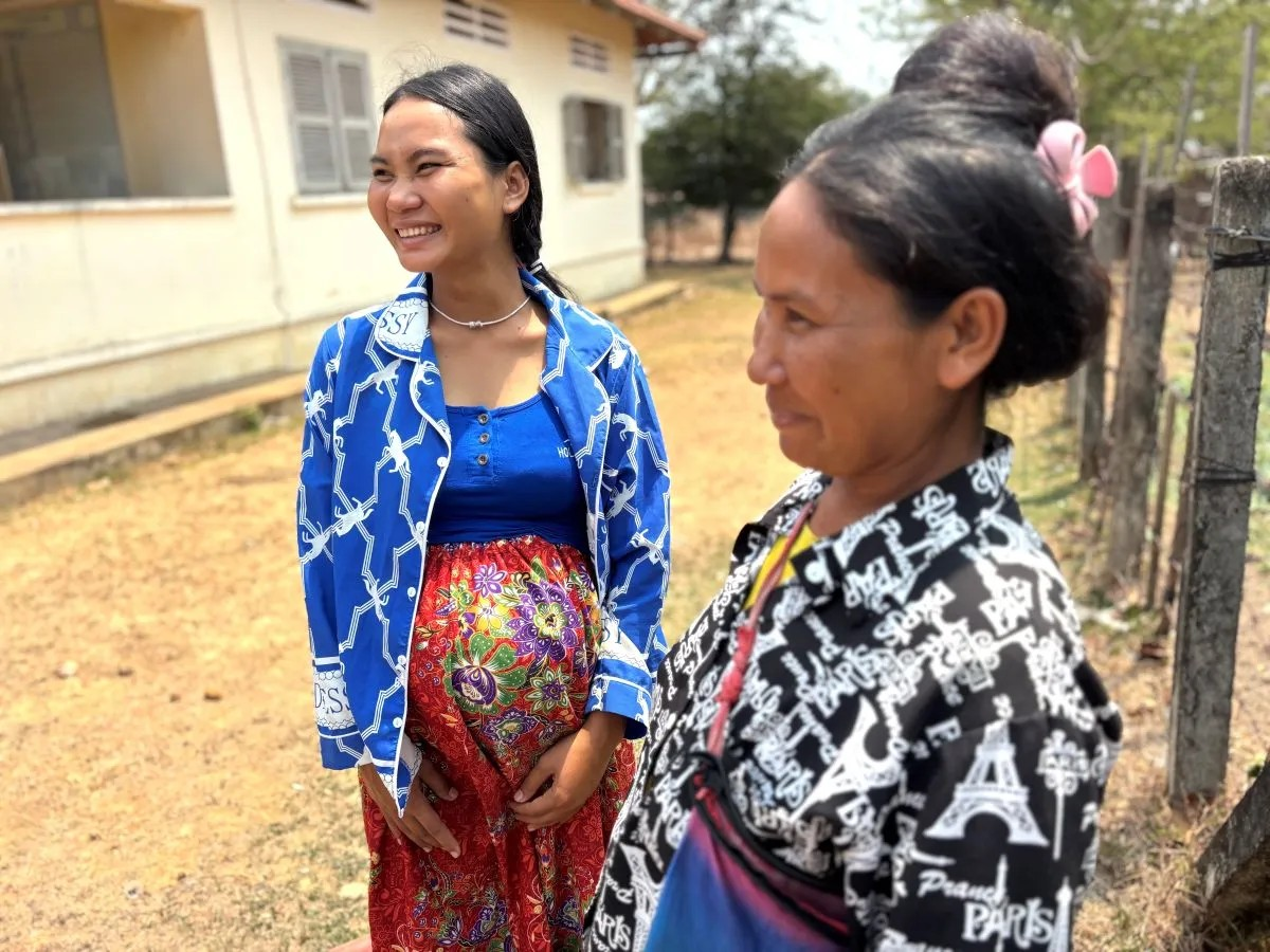 A smiling woman stands beside another woman, both appearing happy and engaged in conversation.