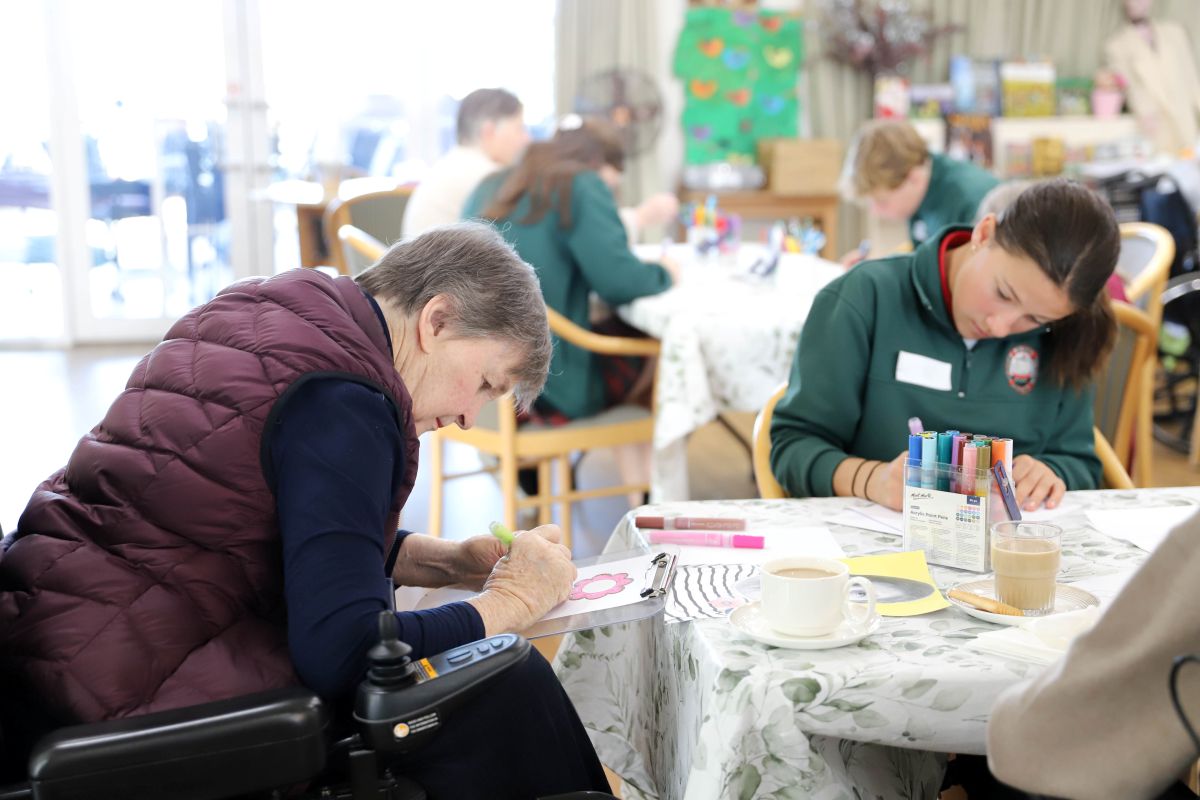 A woman in a wheelchair is drawing alongside a group of people, engaged in a creative activity together.