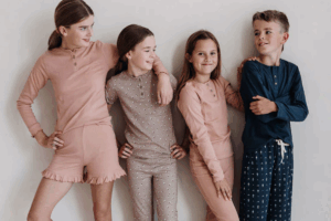 Four children in pajamas, with one leaning against a wall, smiling and enjoying a playful moment together.