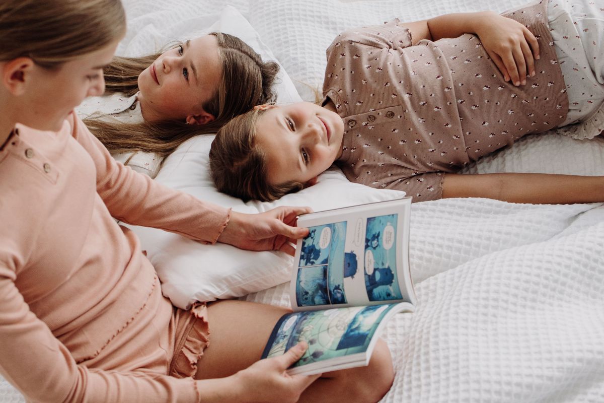 Children lying on a bed, engrossed in reading a book together.