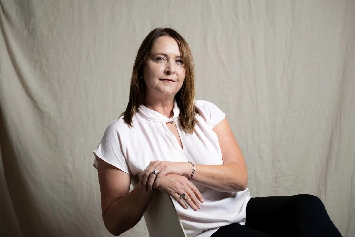 A woman sitting on a chair with her arms crossed, displaying a thoughtful expression.
