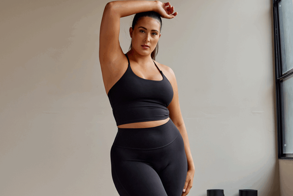 A woman wearing a black sports bra and leggings, standing confidently in a fitness setting.