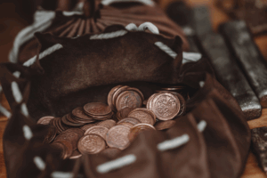 A bag overflowing with coins sits on a wooden table, reflecting light and creating a sense of abundance.