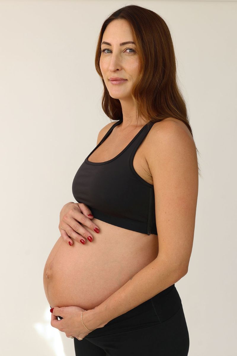 A pregnant woman wearing a black sports bra, showcasing her baby bump while standing confidently.