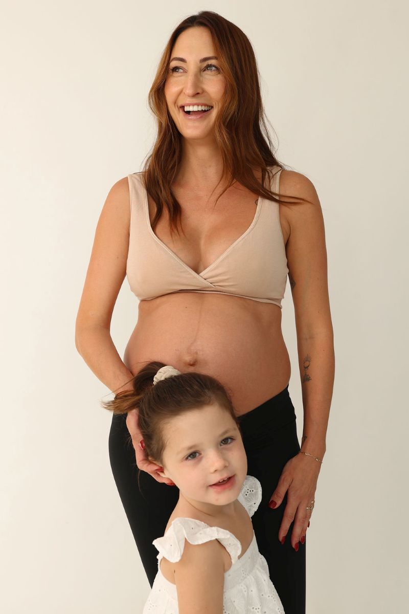  A pregnant woman and her young daughter smiling together for a photo, showcasing their joyful bond.