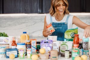 A smiling woman holds a jar of food, showcasing her enjoyment and enthusiasm for the meal inside.
