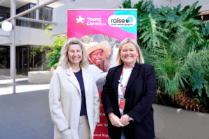 Two women stand beside a pink banner, smiling and engaging with the audience at an event.