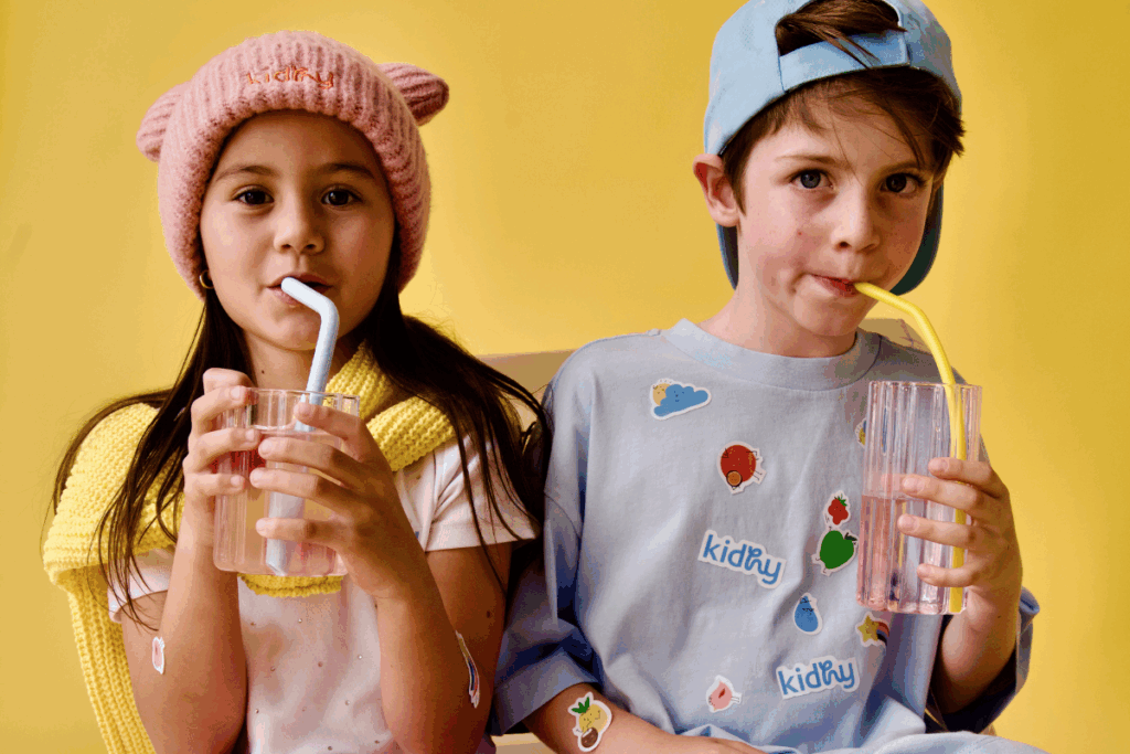 Two children happily drinking from colorful plastic cups.