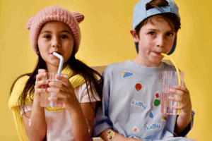 Two children happily drinking from colorful plastic cups.