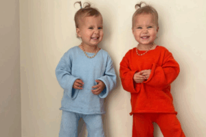 Two young children in matching blue and orange outfits, smiling and standing side by side.