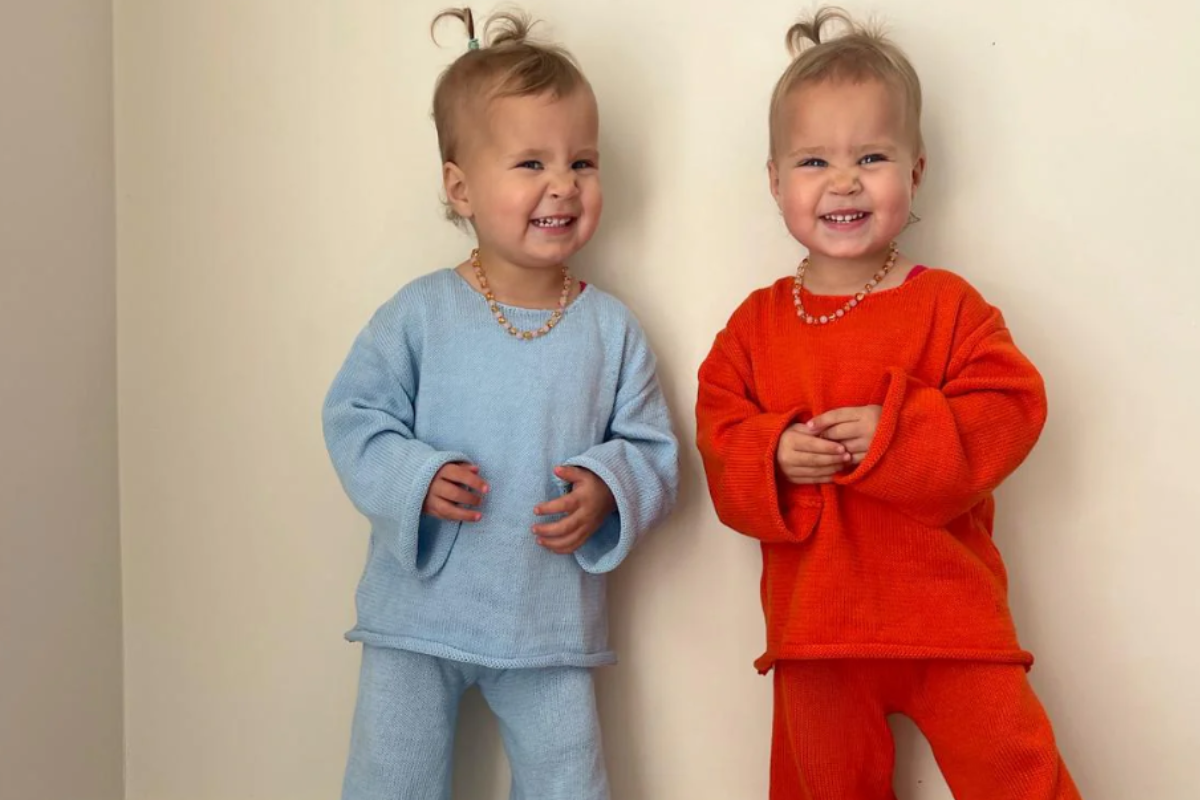 Two young children in matching blue and orange outfits, smiling and standing side by side.
