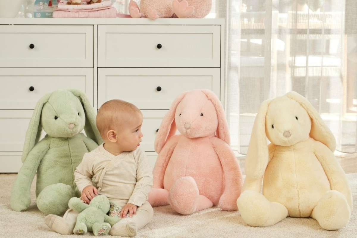 A baby sits on the floor surrounded by various colorful stuffed animals, smiling and playing.
