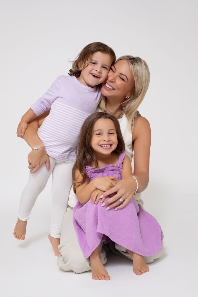 A woman sits on the floor with two children, engaged in a playful activity together.