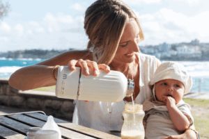 Woman feeding a baby a bottle at the beach.