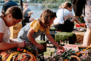 Two young girls are arranging a colorful basket filled with various flowers, focused on their creative task.