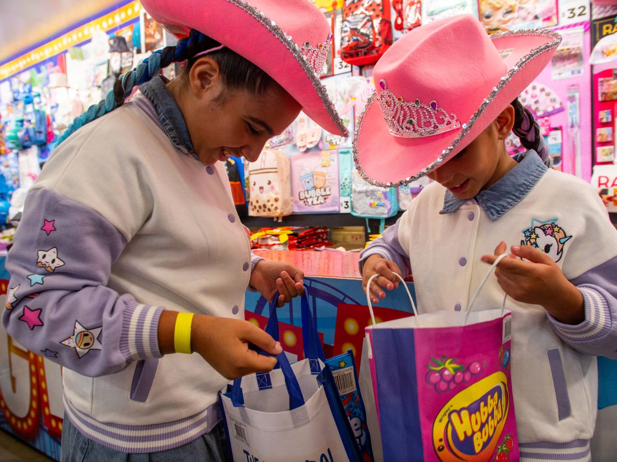 Girls wearing a pink hat, smiling, and peering into show bags.