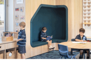Children sitting at desks in a classroom with a vibrant green wall in the background.