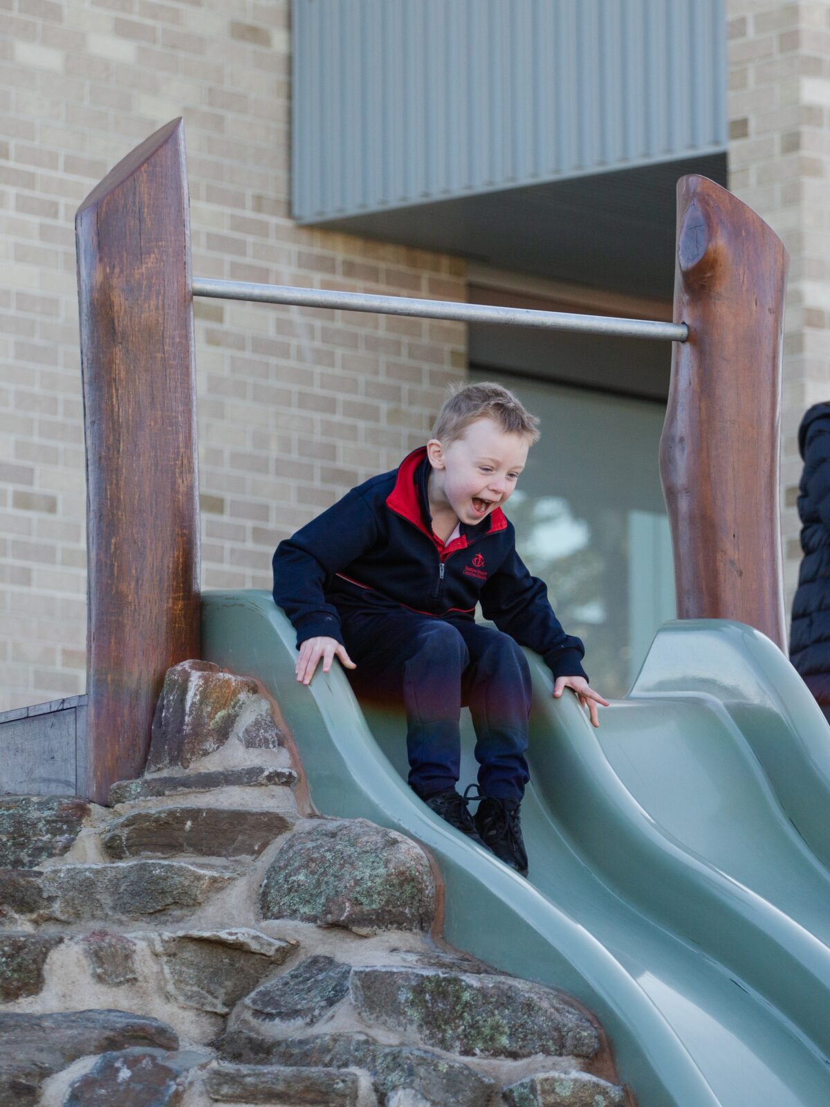 A young boy joyfully sliding down a playground slide on a sunny day.