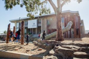 A group of children joyfully playing on a playground next to a building, engaging in various activities.