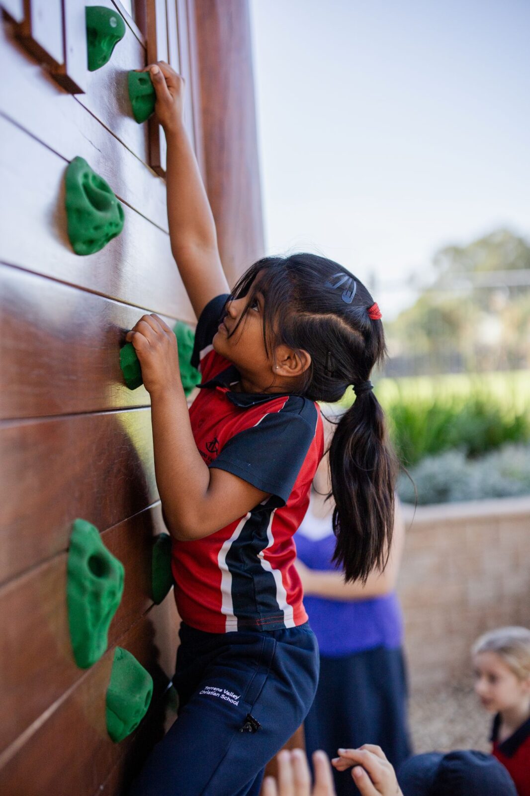 A young girl confidently climbing a colorful climbing wall, reaching for the next hold with determination.