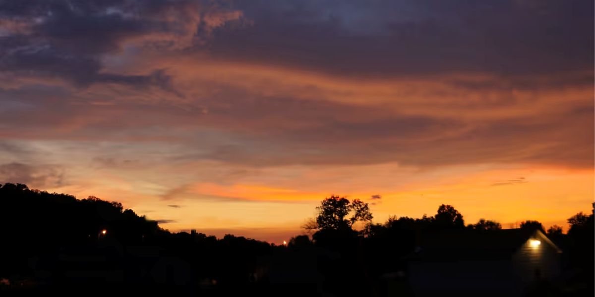 A vibrant sunset casts warm hues over a town, silhouetting houses and clouds against the colorful sky.