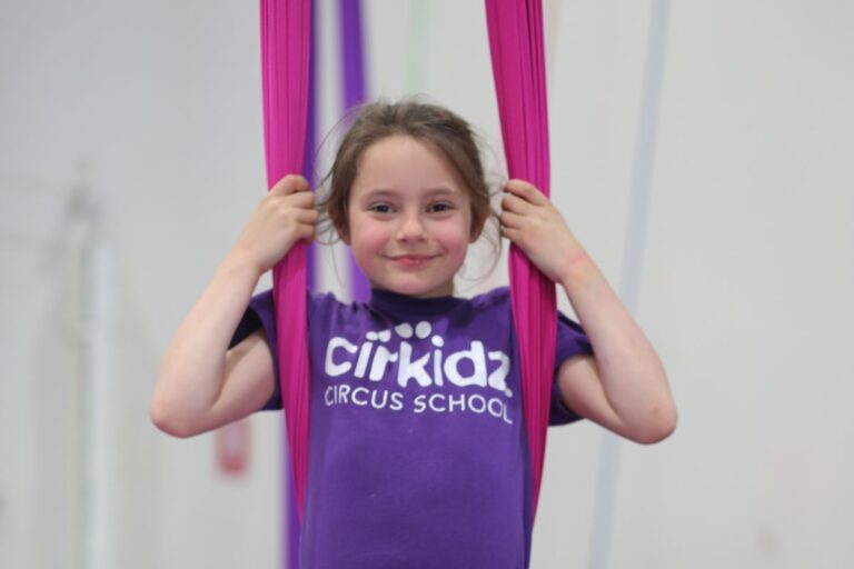 A young girl clutches a purple aerial, highlighting her engagement in an aerial dance or gymnastics activity.