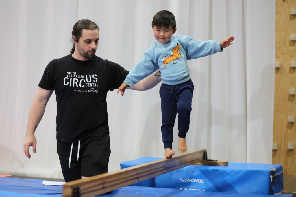 A man and a young boy practice balancing together on a beam, demonstrating teamwork and coordination.