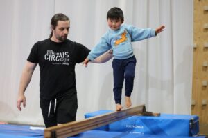 A man and a young boy practice balancing together on a beam, demonstrating teamwork and coordination.