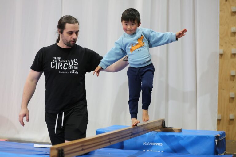 A man and a young boy practice balancing together on a beam, demonstrating teamwork and coordination.