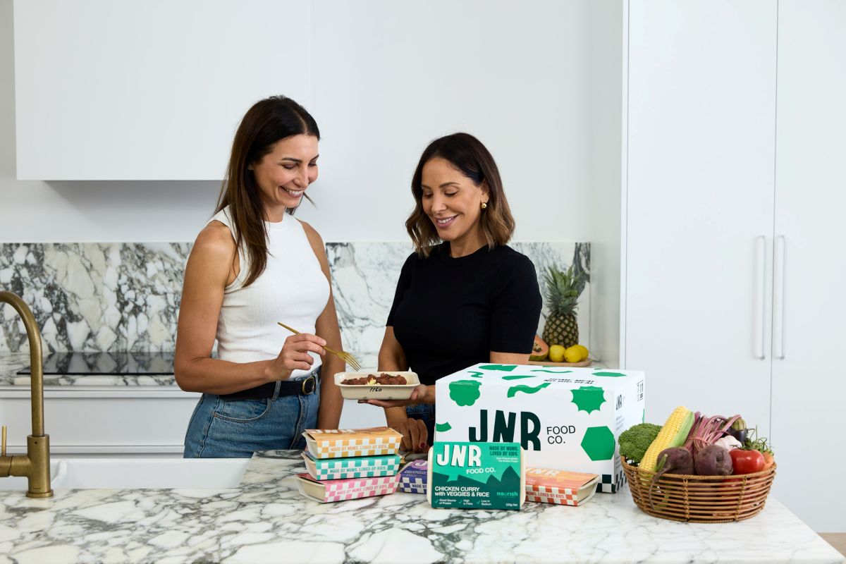 Two women standing in a kitchen, preparing food together with various ingredients on the counter.
