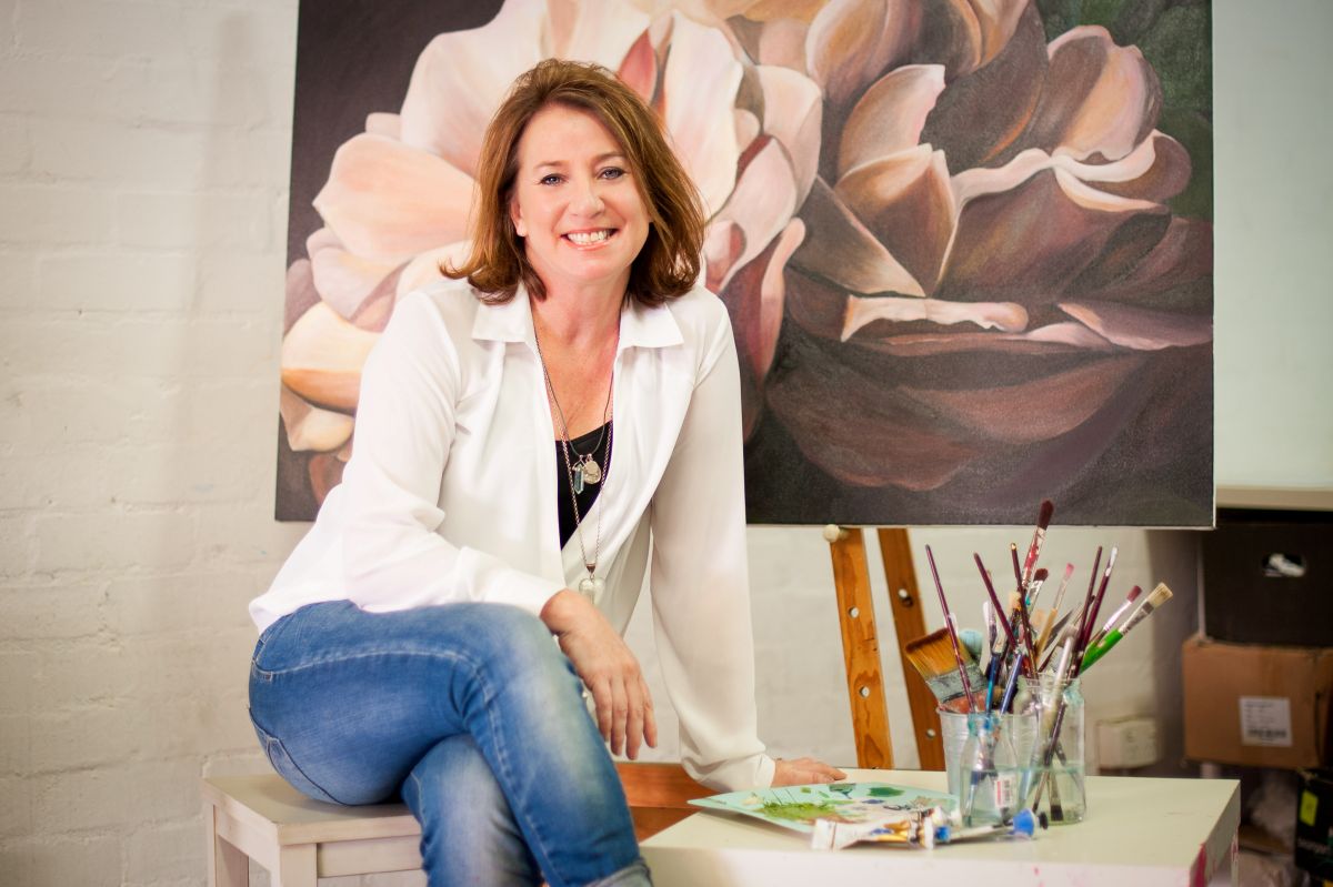 A woman sits on a stool, gazing thoughtfully at a large painting displayed on the wall in an art gallery.