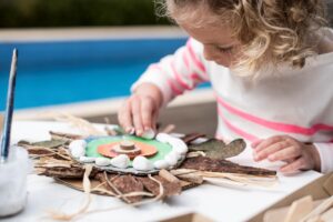 A young girl crafts a flower using leaves and sticks, showcasing her creativity in nature-inspired art.