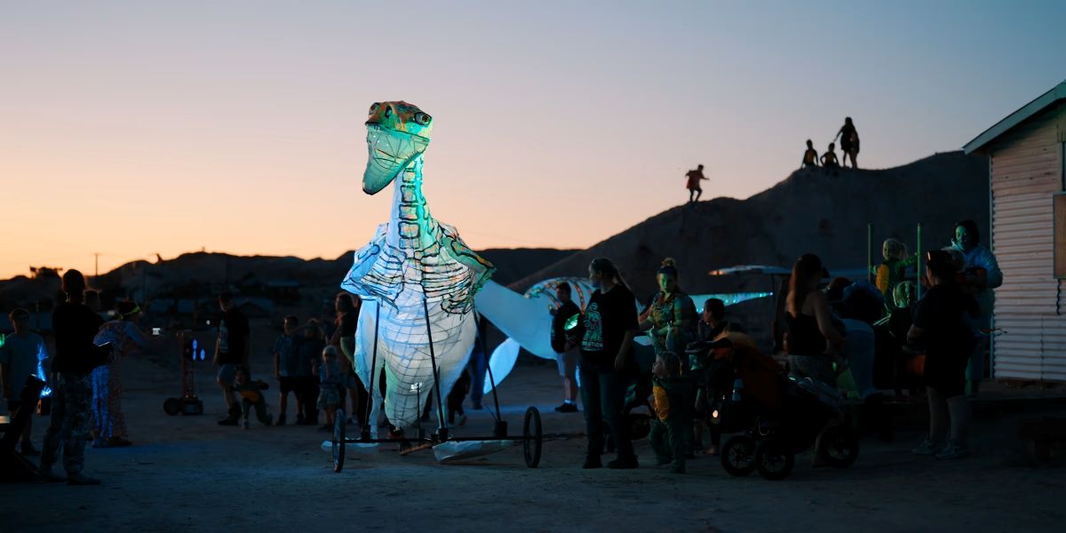 A large bird sculpture illuminated by warm sunset light, casting long shadows on the ground.
