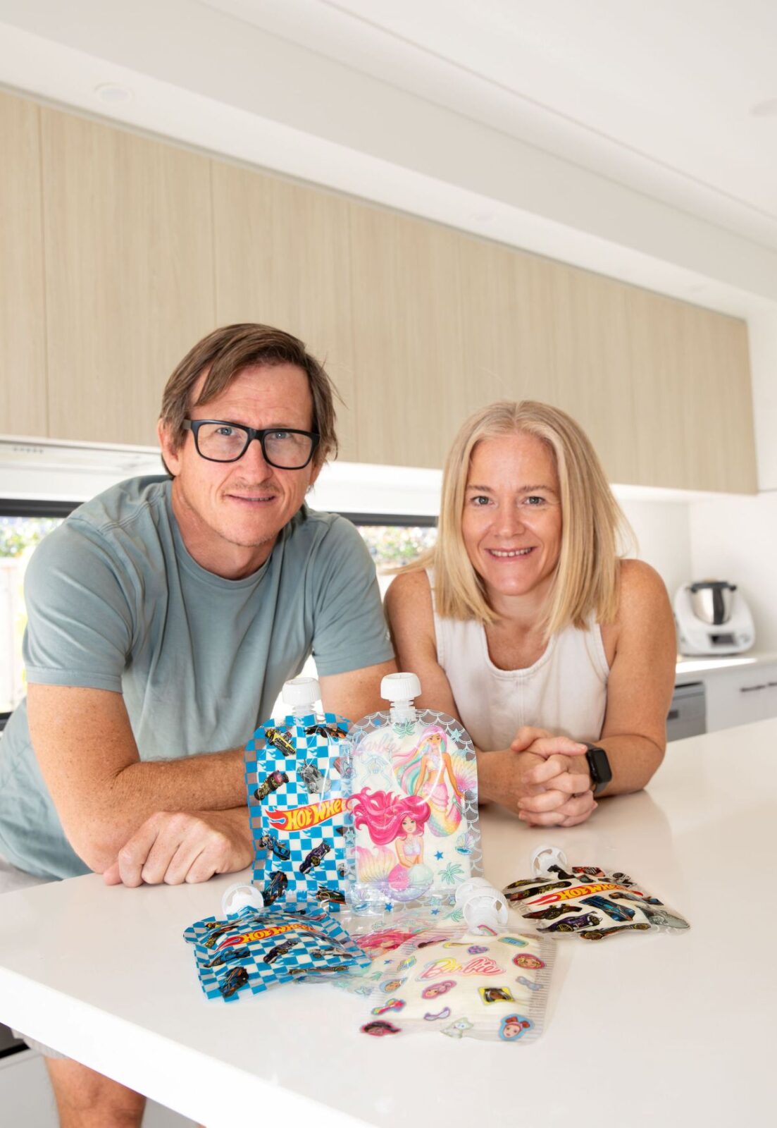  A man and woman sit at a kitchen counter surrounded by food pouches.