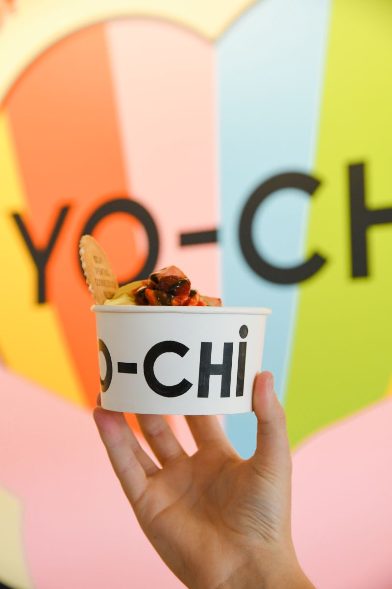  A person holding a cup of yo-chi yoghurt, showcasing a colorful swirl of flavors and a cheerful expression.