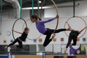 A group of young girls performing gymnastics on rings, showcasing their skills and teamwork in a bright gym setting.