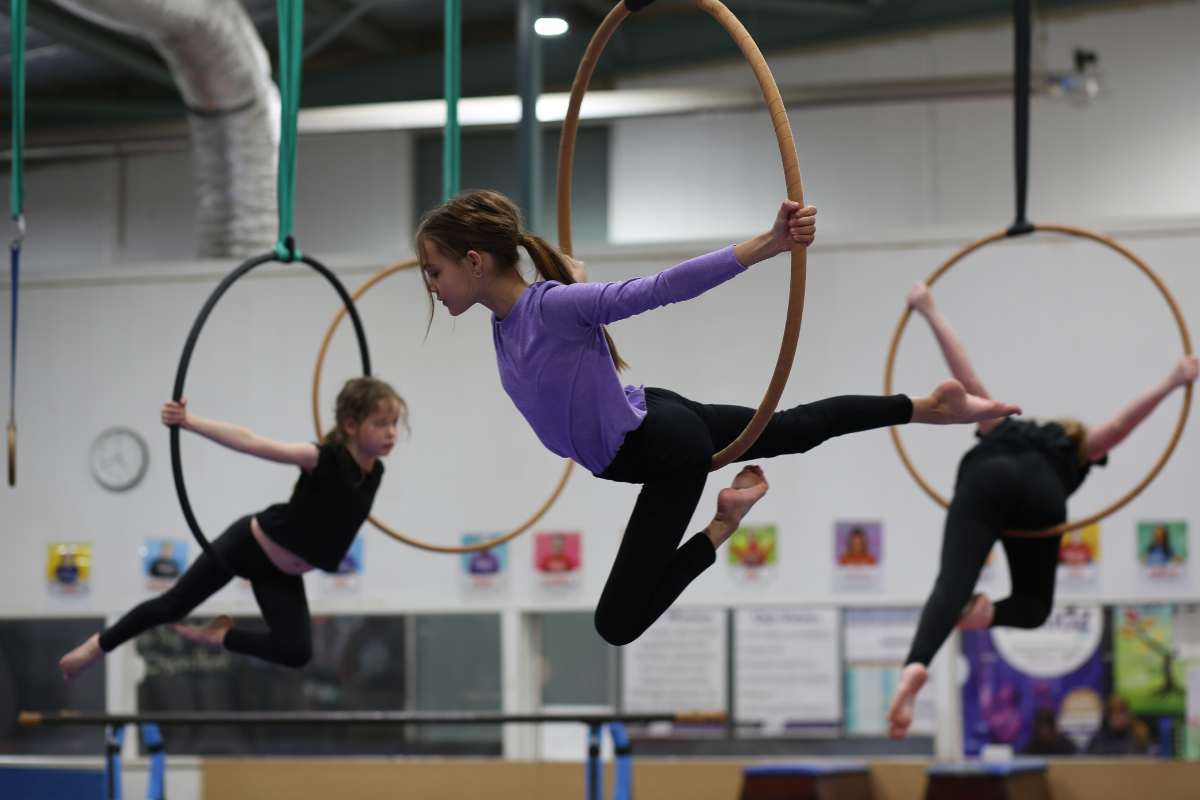 A group of young girls performing gymnastics on rings, showcasing their skills and teamwork in a bright gym setting.