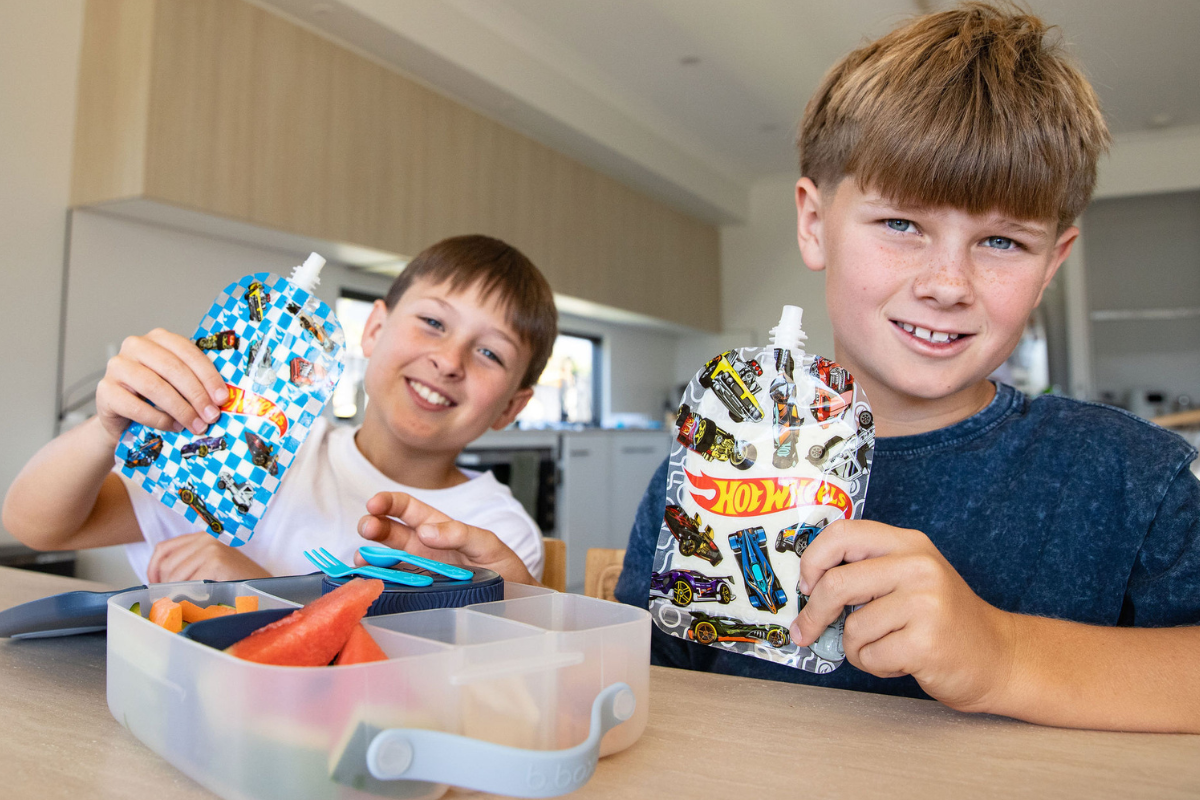 Two boys sitting at a table, sharing a lunch box and enjoying their meal together.
