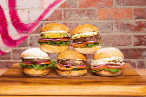 A group of freshly made hamburgers arranged on a wooden cutting board, showcasing their toppings and buns.